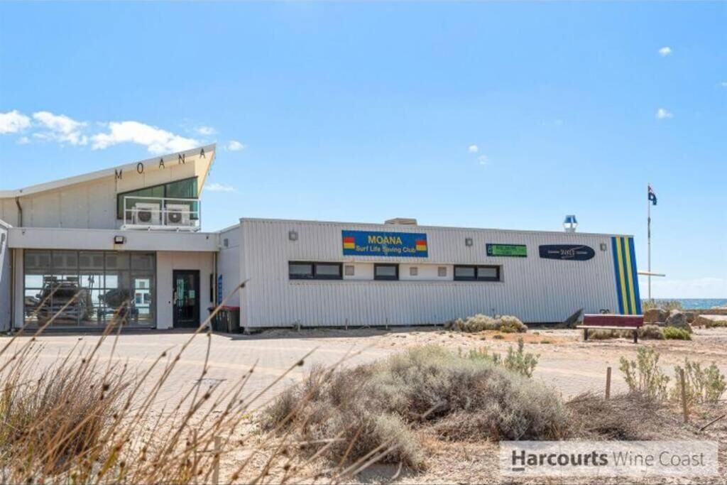 A building with a sign reading "MOANA Surf Life Saving Club" and a flagpole with a flag.