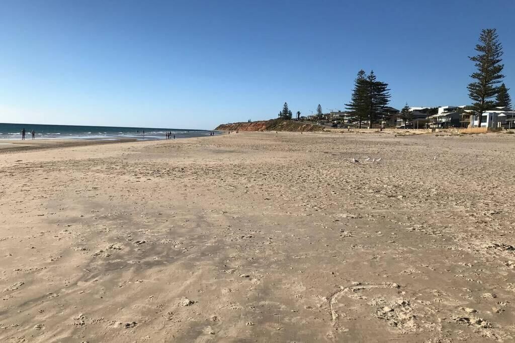 A sandy beach with footprints, a clear sky, and houses in the background.