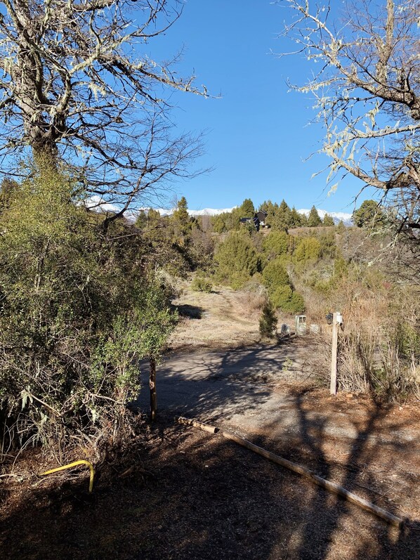 Un paisaje rural con un camino de tierra que lleva a una casa rodeada de árboles y montañas al fondo.