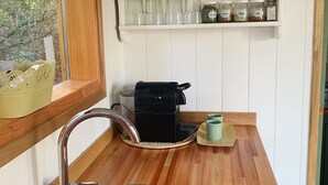 Een keuken met een roestvrijstalen spoelbak, een houten aanrecht en witte planken met glazen potten en kommen.