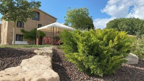 Un edificio de piedra con un patio cubierto, mobiliario exterior y un jardín bien cuidado.