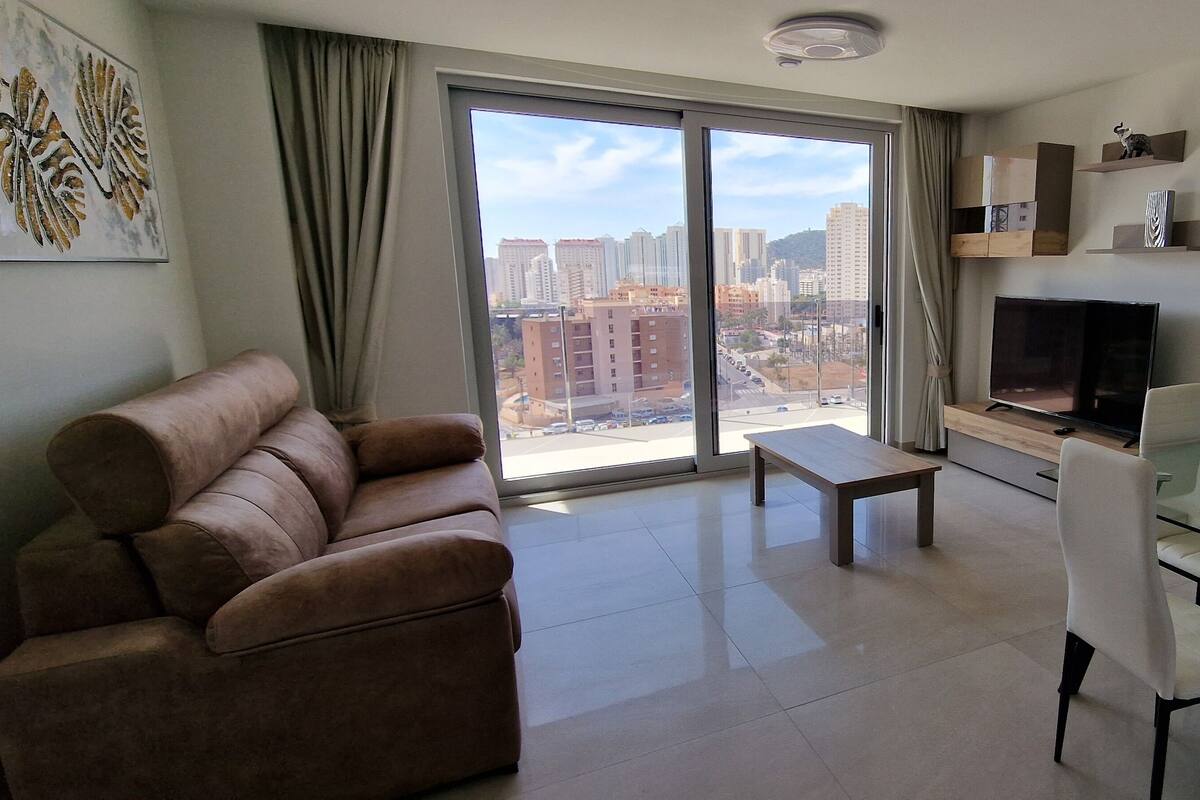 A modern living room with a sofa, a glass dining table, and a TV.
