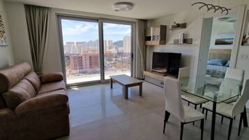 A modern living room with a sofa, a glass dining table, and a TV.