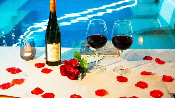 A table with a bottle of wine, two wine glasses, and rose petals.