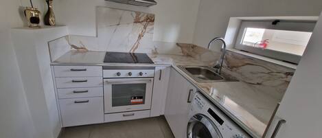 A compact kitchen with a built-in oven, a microwave, a sink, and a washing machine.