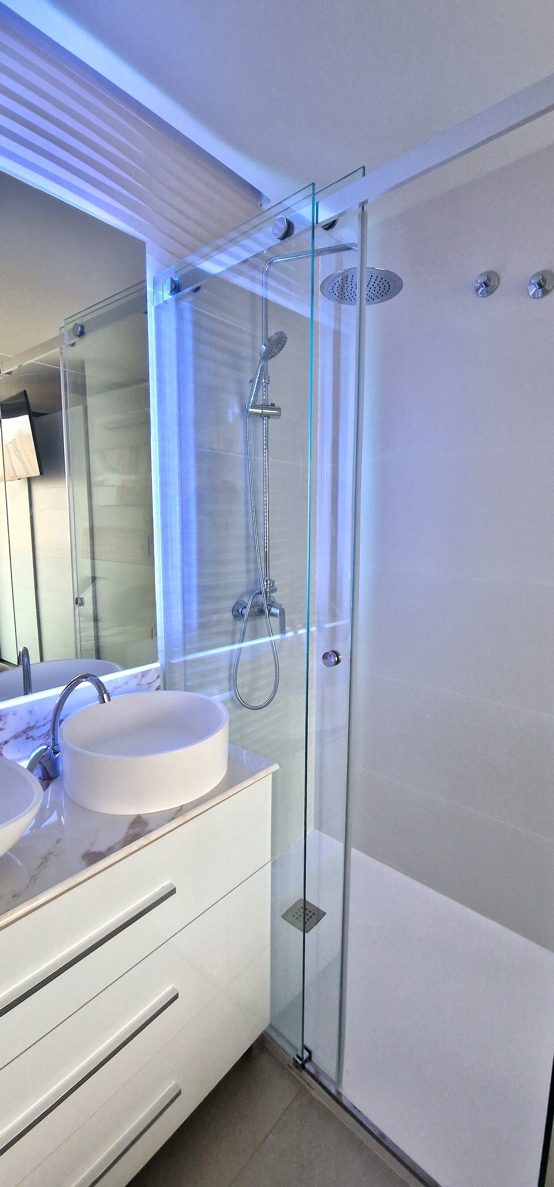 Un baño moderno con ducha de vidrio, un lavabo blanco y encimera de mármol, y un espejo grande.