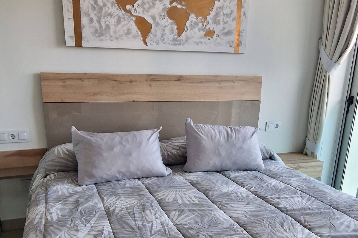 A modern bedroom with a large bed, a wooden headboard, a world map artwork, and an air conditioning unit.