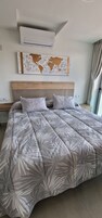 Quarto moderno com uma cama grande, cabeceira de madeira, obra de arte com um mapa mundi e um aparelho de ar condicionado.