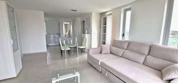 A modern living room with a beige sofa, a glass coffee table, and a dining area with chairs and a table.