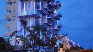 A multi-story hotel with balconies, palm trees, and a clear sky.
