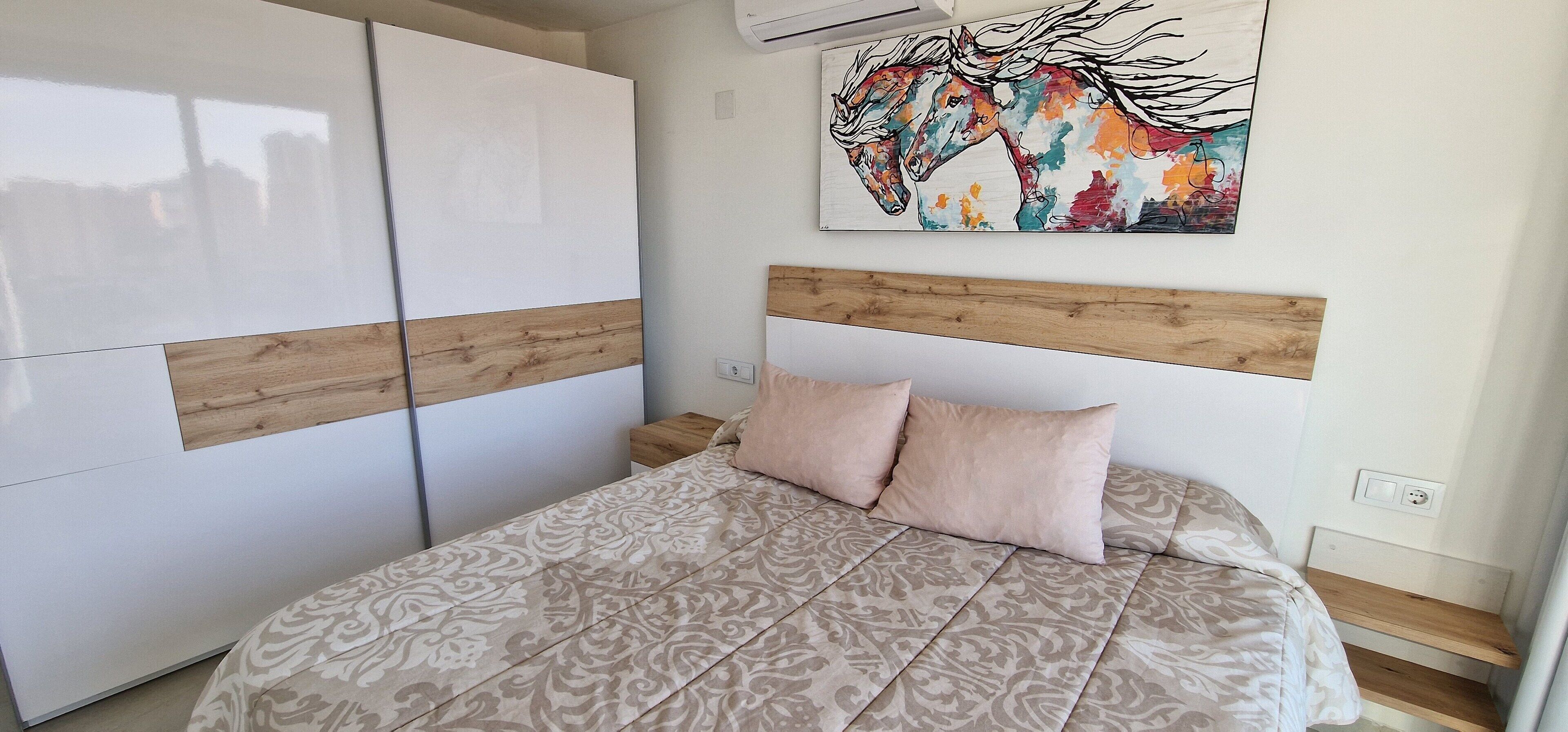 A bedroom with a bed, a nightstand, a wardrobe, and a wall-mounted painting.