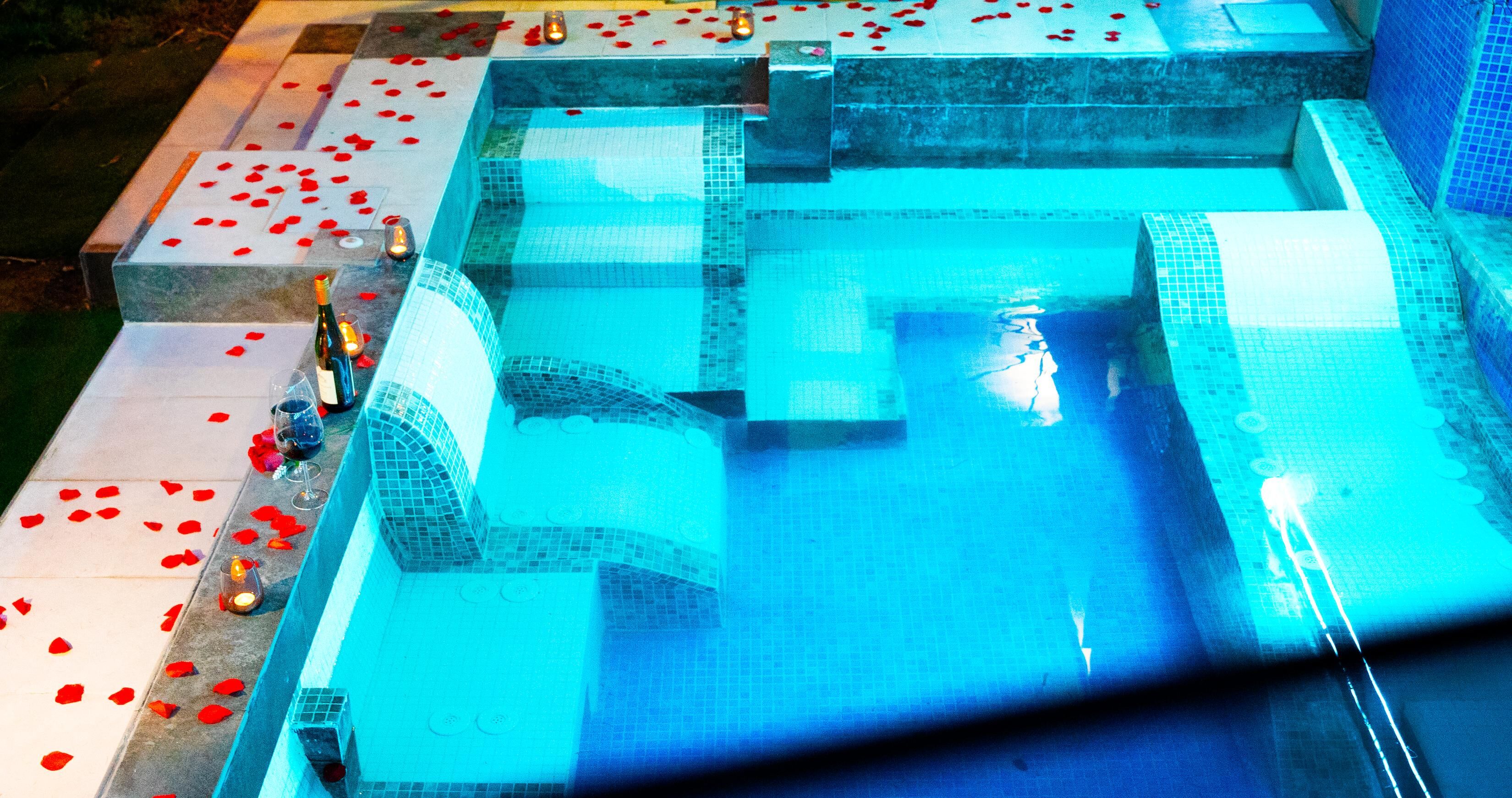 Una piscina con revestimiento de azulejos y escalones de acceso, rodeada de pétalos de rosa esparcidos.