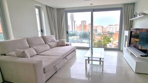 A modern living room with a beige sofa, a glass coffee table, and a flat-screen TV on a white stand.