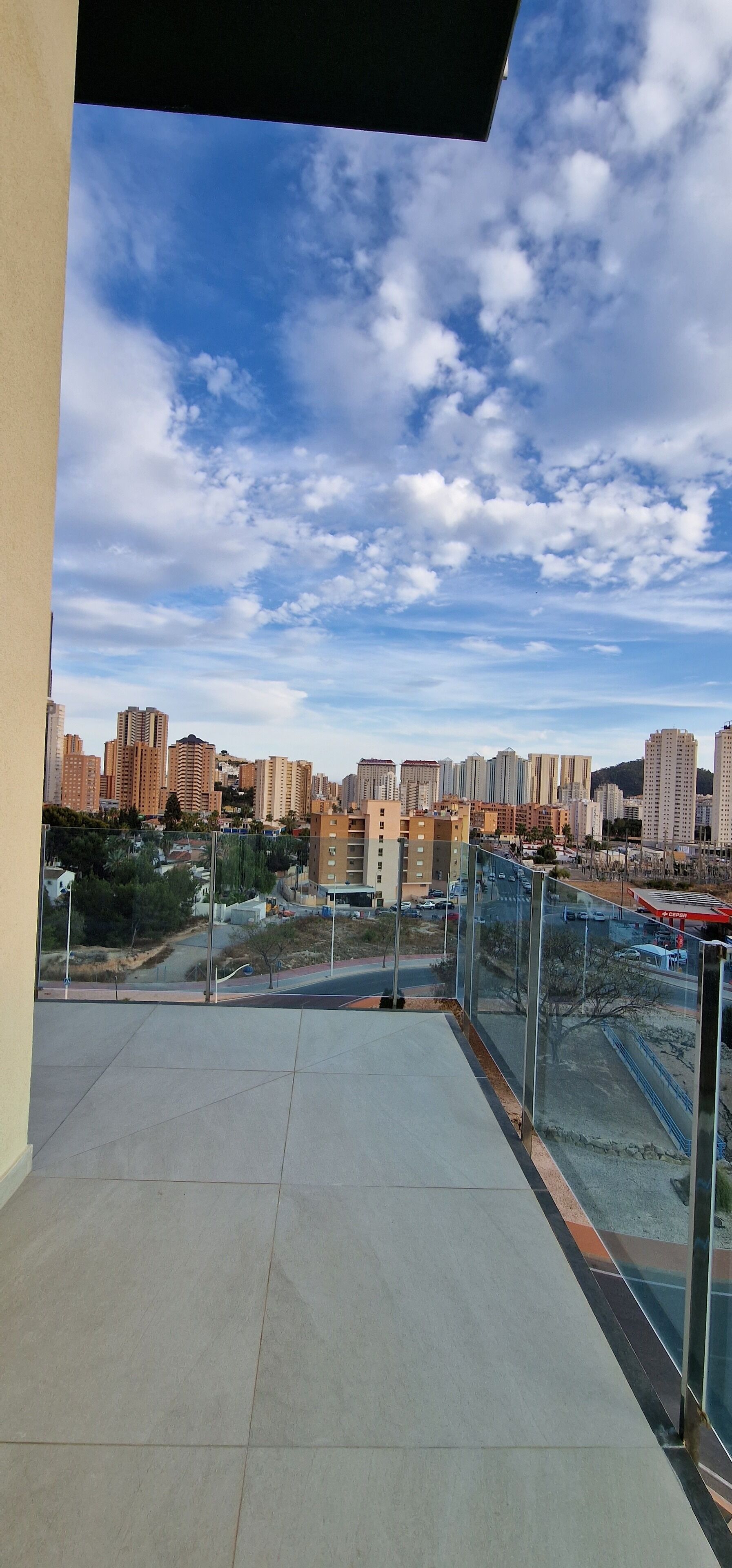 A balcony with a city view, featuring high-rise buildings, a clear sky, and a fenced area.