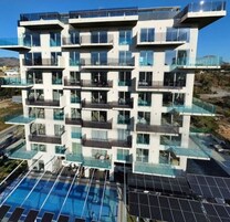 A modern multi-story building with balconies, a rooftop pool, and solar panels.