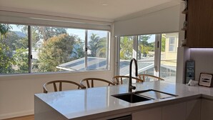 A modern kitchen with a central island, a dishwasher, and a view of the neighborhood. - Cozy House in Forresters Beach - modern interiors  (Forresters Beach)