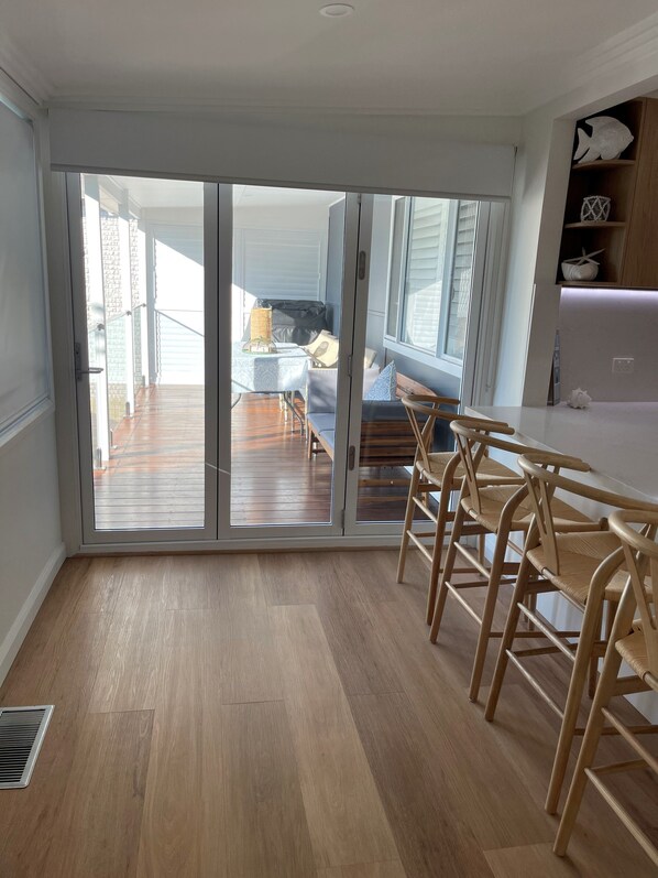 Una cuina moderna amb terres de fusta, una zona de menjador amb taula i cadires, i vista cap a una terrassa exterior a través de grans portes corredisses de vidre.