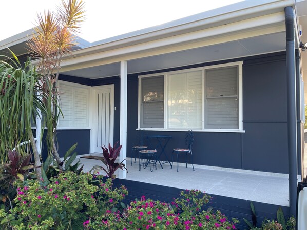 A house with a covered porch, white-framed windows, and a small patio area with chairs. - Cozy House in Forresters Beach - modern interiors (Forresters Beach)