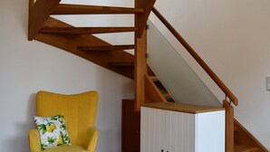 A modern interior with a wooden staircase, a yellow armchair, and a white cabinet. - New 2 room apartment in Murnauer Moos (Schwaigen)