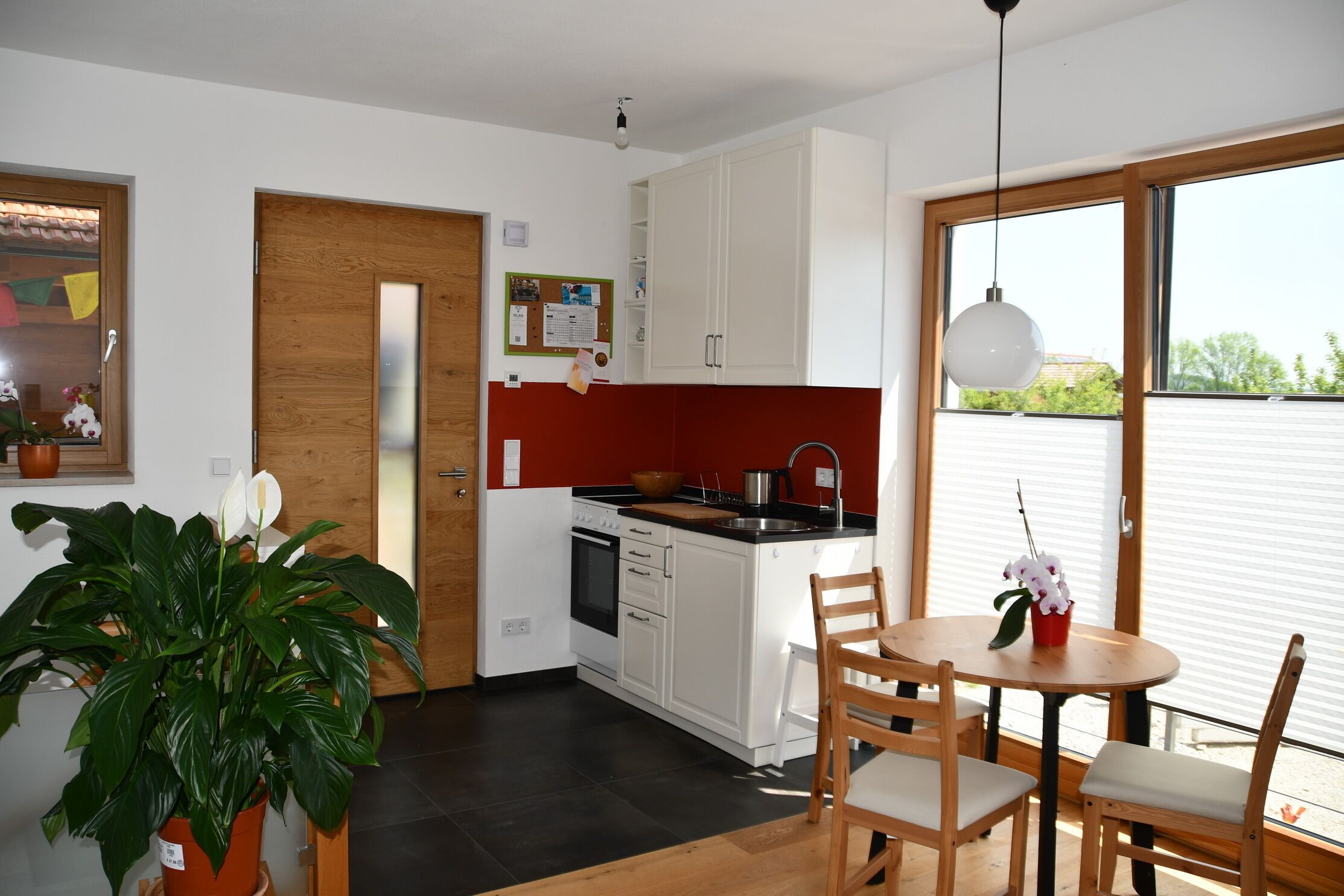 A modern kitchen with white cabinets, a wooden door, and a dining area with a table and chairs.