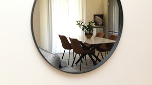 Espelho redondo refletindo uma sala de jantar com mesa, cadeiras e um vaso com flores.