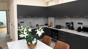 Cozinha moderna com armários escuros, bancada de mármore e área de jantar com um vaso de flores.