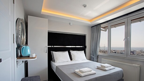 A modern hotel room with a large bed, a view of the city, and a small seating area. - Carvan Hotel (Istanbul)