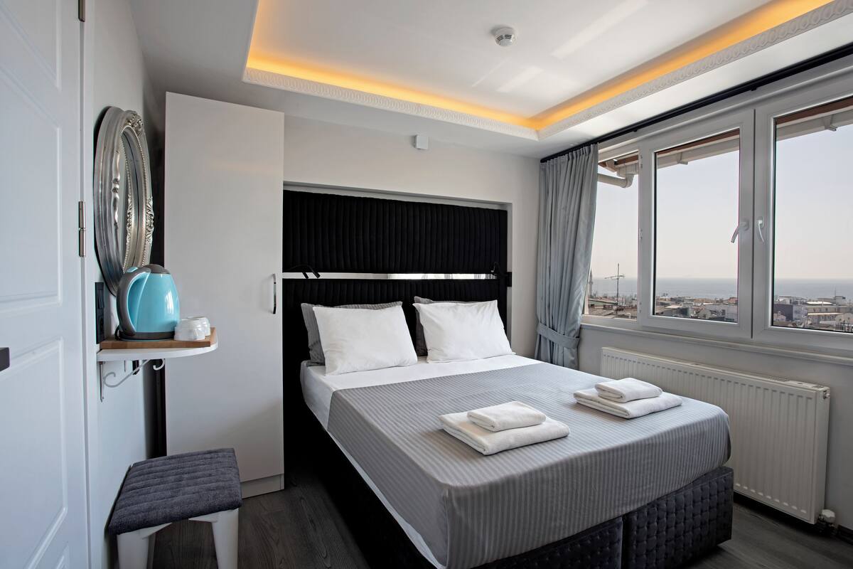 A modern hotel room with a large bed, a view of the city, and a small seating area.