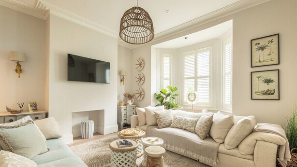Ein Wohnzimmer mit einem beigefarbenen Sofa, einem gemusterten Teppich und einem an der Wand montierten Fernseher.