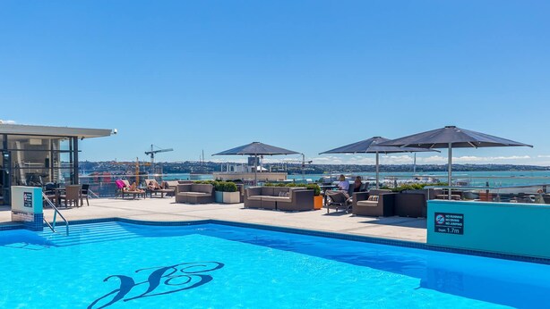 A rooftop pool with lounge chairs and umbrellas, a clear view of the sea, and a sign indicating no running or jumping. - Comfort Studio Getaway with Pool and Gym (Auckland)