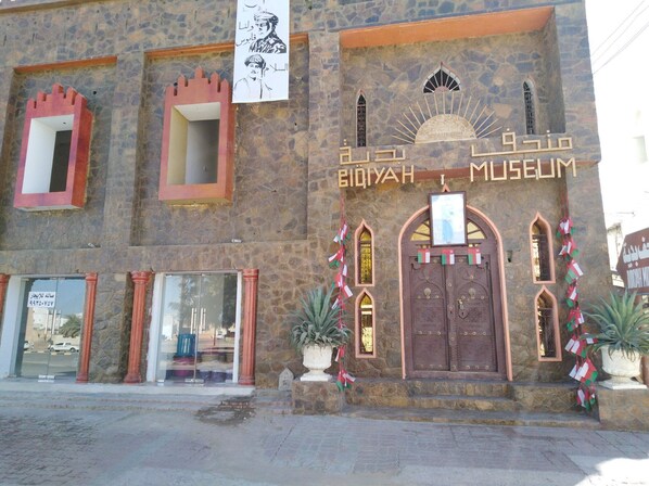 Un edificio con fachada de piedra, una entrada arqueada grande y un cartel que dice "BIQAIH MUSEUM".