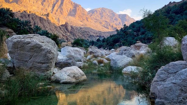 Paesaggio montuoso con un ruscello limpido, circondato da grandi massi e vegetazione.
