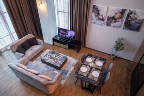A modern living room with a sofa, coffee table, dining table set for four, and a flat-screen TV. - Maritime Suites by The Only Bnb (George Town)