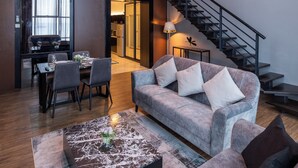 A modern living room with a sofa, coffee table, and dining area. There is a staircase leading to an upper level.