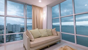 A modern living room with a beige sofa, large windows, and a view of a cityscape.