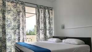 A bedroom with a bed, white pillows, a blue blanket, and a window with patterned curtains. - Sunrise Negombo by Celestial Ceylon (Negombo)