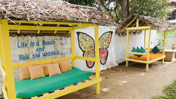 A beach-themed outdoor seating area with a mural, a thatched roof, and a sandy ground. - Sunrise Negombo by Celestial Ceylon (Negombo)