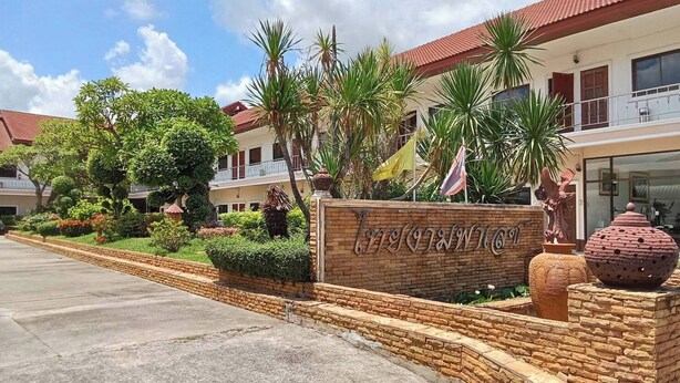 Entrada de hotel con un cartel, un sendero pavimentado y un jardín ajardinado con palmeras y arbustos.