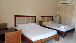 Habitación de hotel con dos camas individuales, una silla de madera, una mesa y un equipo de aire acondicionado.