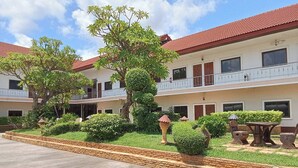 Un hotel de varios pisos con tejado de tejas rojas, un jardín ajardinado con diversas plantas y un camino pavimentado.