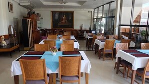 Un comedor con mesas dispuestas para recibir a los huéspedes, sillas de madera y un cuadro de Buda en la pared.