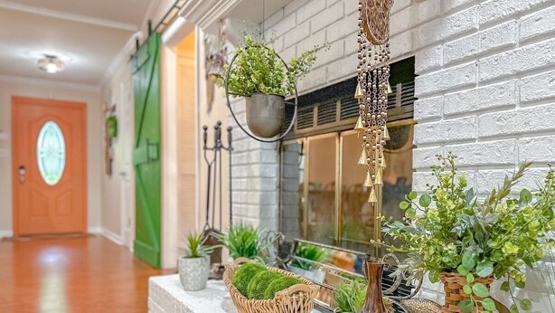Un couloir doté d’un plancher en bois, d’une cheminée en briques blanches, ainsi que de différentes plantes en pot et de paniers disposés sur le manteau de la cheminée.