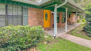 Une maison à deux étages avec un porche couvert, une porte jaune et une façade en briques.