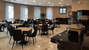 Un espacio interior amplio con varias mesas y sillas, una máquina de café y un mostrador con caja registradora.