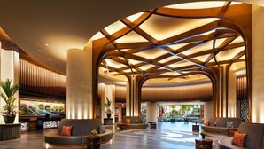 Um hall amplo com design moderno, apresentando uma área de estar em curva, um balcão de recepção e um espaço amplo e aberto com uma estrutura de teto singular.