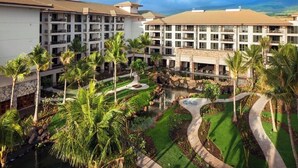 Um resort com edifícios de vários andares, um pátio central com um elemento aquático e palmeiras.