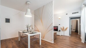 A modern dining area with a white table, metal chairs, and a pendant light. A decorative wall with a leaf pattern is visible. - RESIDENZA BELLA VITA (Modena)