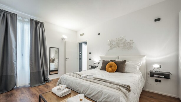 A modern hotel room with a large bed, a bedside table with a lamp, a mirror, and a view of the hallway. - RESIDENZA BELLA VITA (Modena)