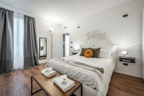 Et moderne hotelværelse med en stor seng, et sengebord med lampe, et spejl og udsigt til gangen.