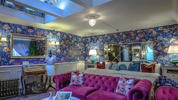 A room with a floral wallpaper, a large mirror, a tufted sofa, and a ceiling fan.